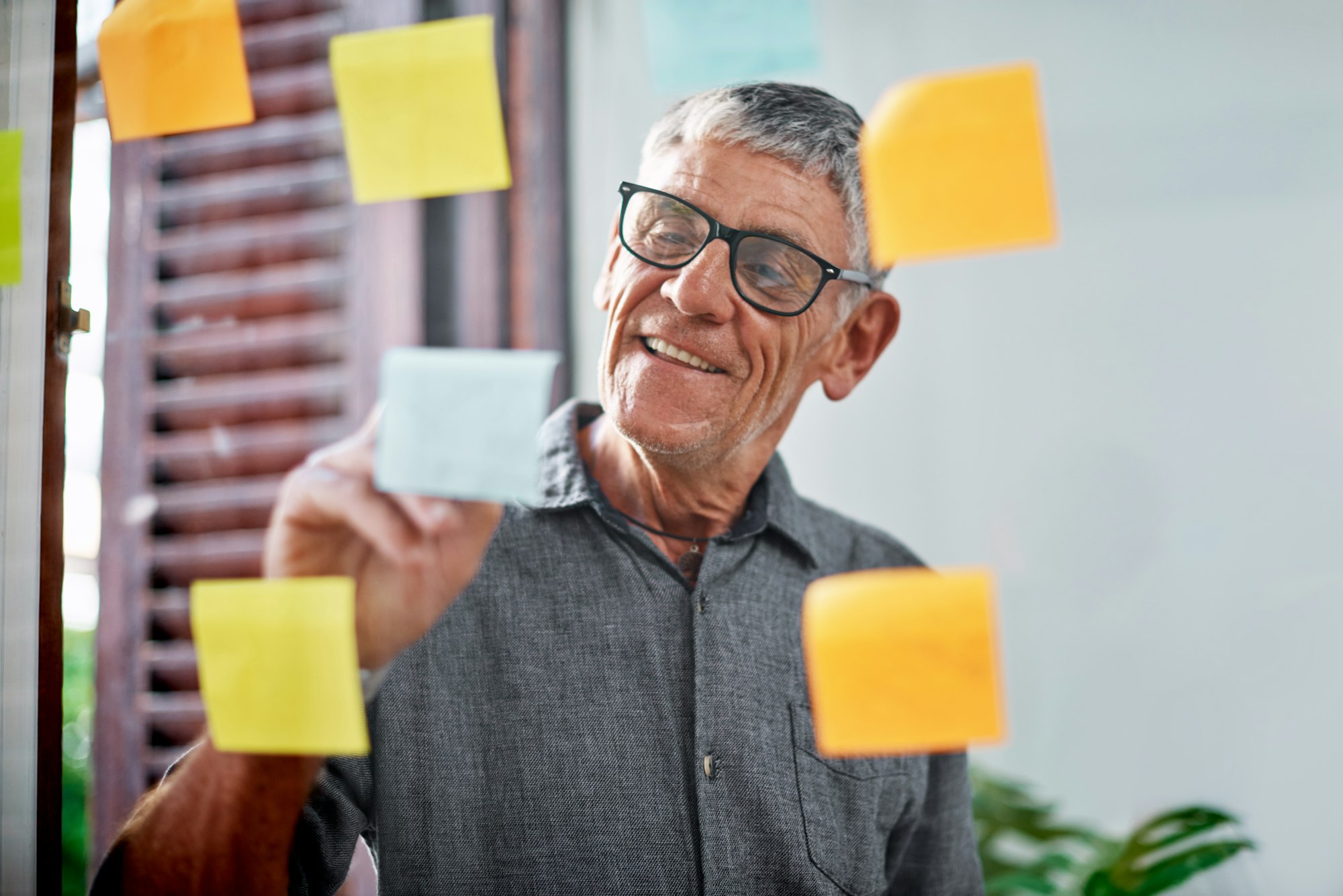 Shot of a senior businessman brainstorming with notes on a glass wall in an office